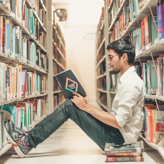 person sitter på golvet mellan två bokhyllor i ett bibliotek